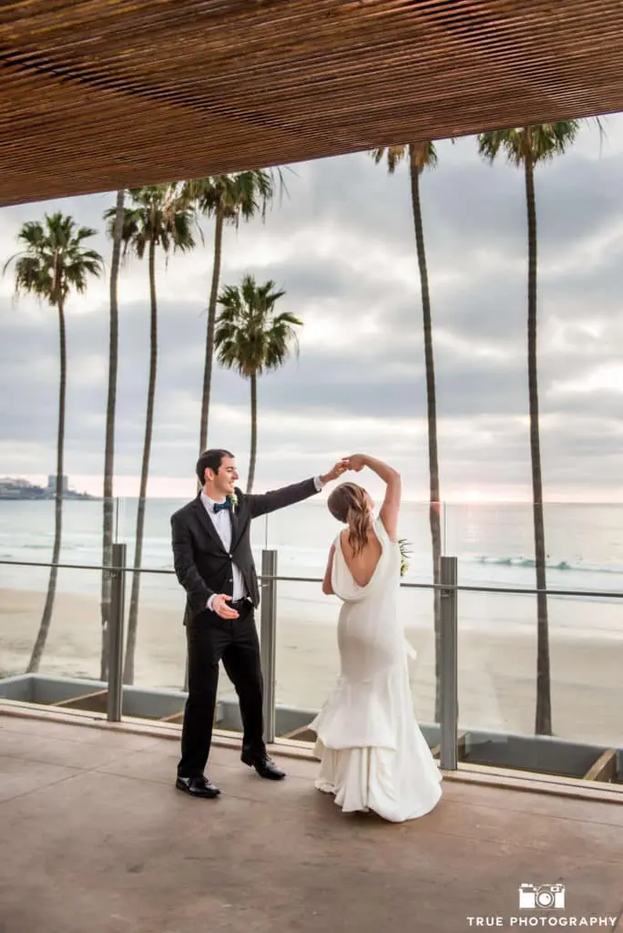 The groom spins the bride on the balcony overlooking the ocean view.