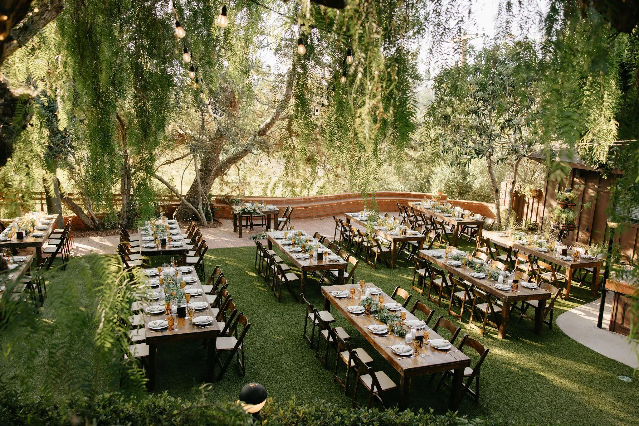 Rustic outdoor seating arrangement with wooden tables and chairs on a grassy lawn, decorated with floral centerpieces for a catered event