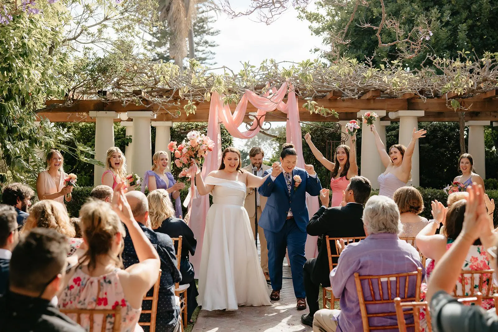 Joyful wedding couple celebrating their outdoor ceremony with friends and family cheering and applauding