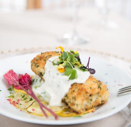 San Diego wedding catering dish: Herb-crusted fish fillet topped with creamy sauce, accompanied by microgreens and garnished with a splash of edible flowers on a white plate