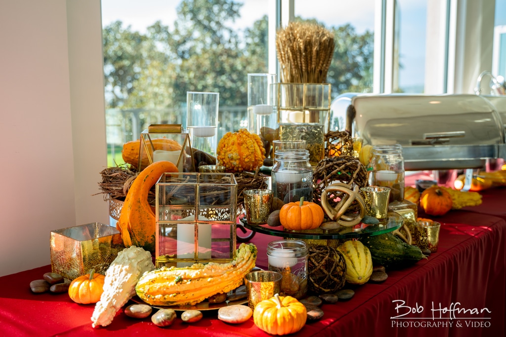 Festive autumn-themed table setting featuring an array of pumpkins, gourds, decorative jars, candles, and natural elements, with a backdrop of a bright window