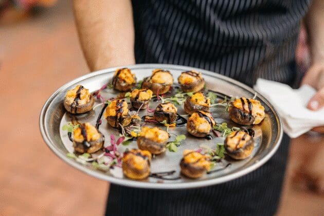 Server presenting stuffed mushroom bites with balsamic drizzle, a cozy autumn appetizer for receptions