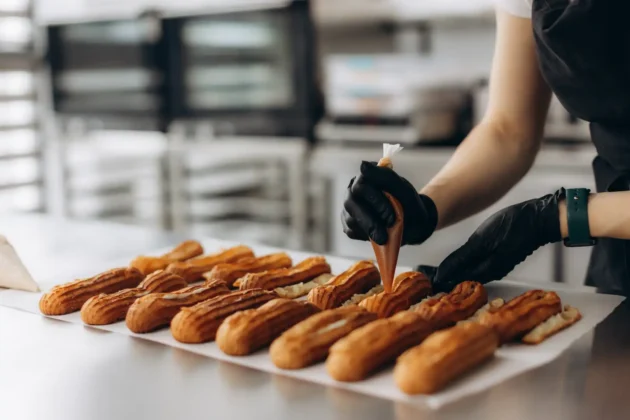 Baker piping cream into fresh eclairs, representing artisan pastry making, bakery food preparation, and professional dessert catering.